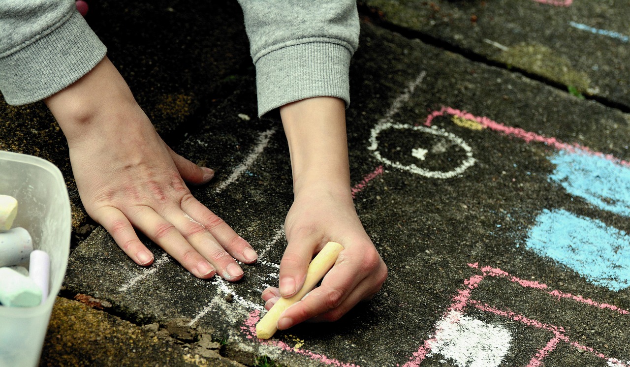 Mani di un bambino che disegna con gessetti colorati all’aperto